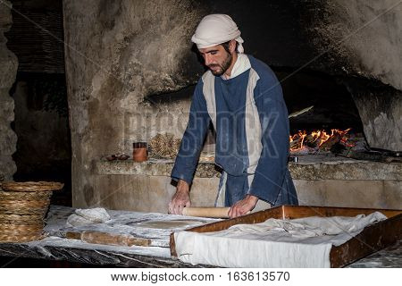 NAZARETH ISRAEL - DECEMBER 16: Man dressed in period clothes rolls the dough with rolling pin in Nazareth Village Israel on December 16 2016