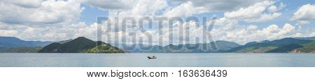 Single boat moving on Lugu Lake surrounded by mountains under cloudy sky, in Lijiang, Yunnan, China