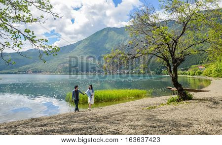 Young Chinese couple having fun while walking along the bank of Lugu lake hand in hand, at Daluoshui village, Lijiang, China