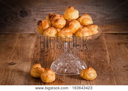Sweet cream puffs on glass tray on wooden table.