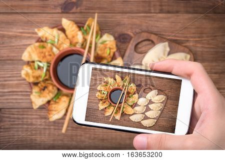 Hands taking photo homemade сhicken potstickers with soy sauce with smartphone.