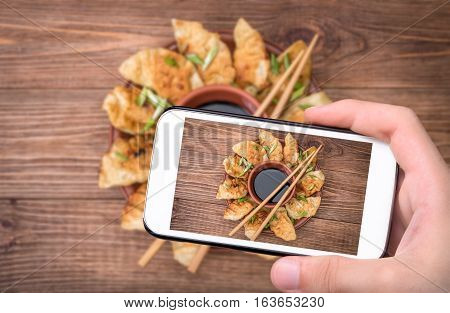 Hands taking photo homemade сhicken potstickers with soy sauce with smartphone.