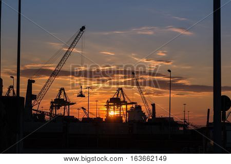 Silhouette of Cranes at Work in Boatyard at Sunset