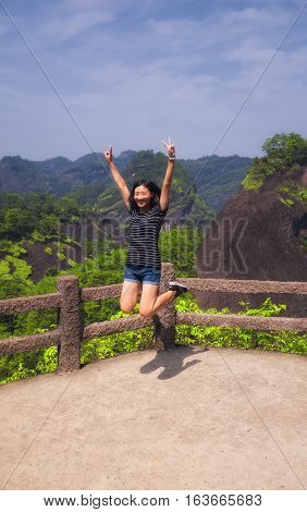 A chinese woman jumping for joy on a platform within the wuyishan scenic area in Fujian province china.