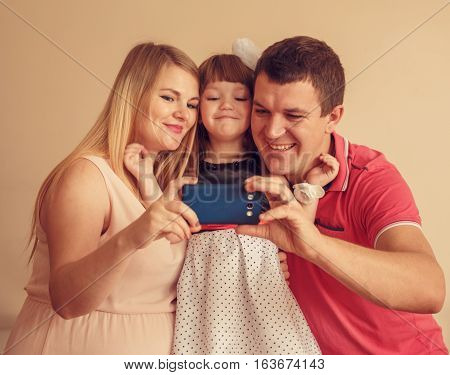 Man with woman and girl use a smartphone to take a salf photo together