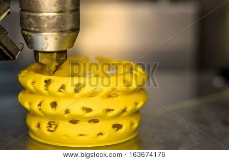 3D printer prints yellow form figure close. Automatic three dimensional 3d printer performs plastic modeling in laboratory. Plastic Wire Filament on 3D Printer. Modern printing technology.