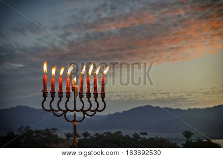 Menorah with glitter lights of candles is traditional symbol for Jewish Hanukkah Holiday
Photo was taken at sunrise using the nine burning decorative candles as foreground for inspiration of Jewish symbols for Hanukkah holiday. Selective focus