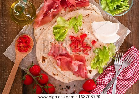 Piadina with ham and lettuce on baking paper.