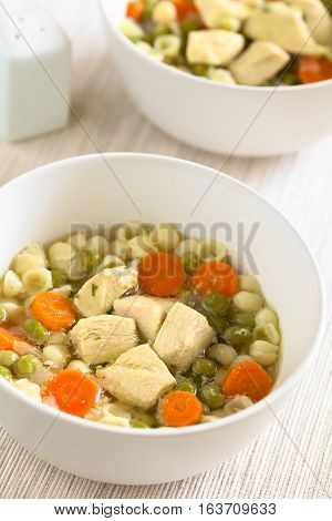 Homemade chicken soup with pea carrot and small shell pasta in bowls photographed with natural light (Selective Focus Focus in the middle of the first soup)