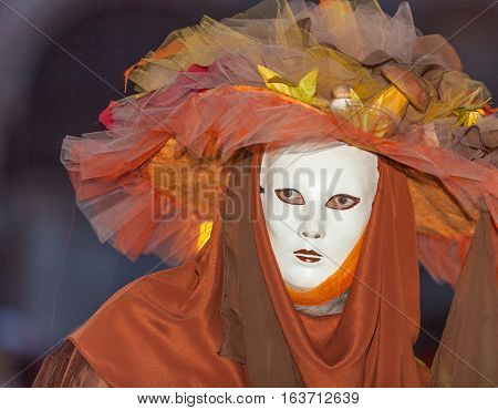 Venice Italy- February 26th 2011:Environemntal portrait of a person wearing a specific orange costume and a mask during the Venice Carnival nights.