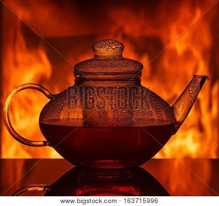 A glass teapot at the table in front of a fireplace