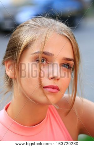 Pretty young woman or girl with tied in bun blonde hair in pink shirt with cute face on sunny day