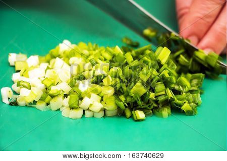 Woman chopping green onion with knife on the table in the kitchen. Healthy eating, cooking, vegetarian food.