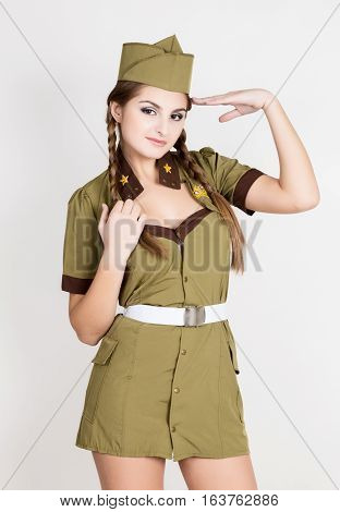 sexy fashionable woman in military uniform and forage-cap, put a hand to her head and salutes.