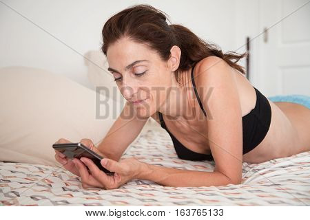 Smiling Woman Lying On The Bed Watching Smartphone