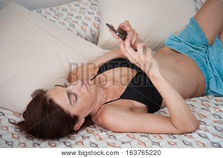 Woman Lying On The Bed Face Up Using Mobile Phone