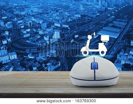 Wireless computer mouse with motor bike icon on wooden table over aerial of city tower street and expressway Business internet delivery service concept