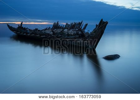 Old broken boat wreck on the shore a frozen sea and beautiful blue sunset background. Estonia Europe.