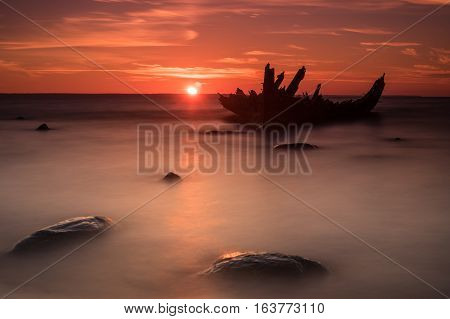 Old broken boat wreck on the shore a frozen sea and beautiful red sunset background. Estonia Europe.