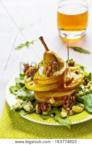Fruit salad whole pear sliced walnuts caramelized in honey blue cheese and arugula. Green plate on white wooden table.