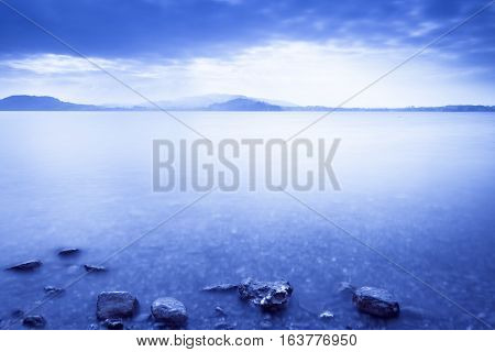 Sunset Lake. On a background the mountains. Tops of stones in water. Play of light and shadow creates a gorgeous volume and distance. Long exposure.