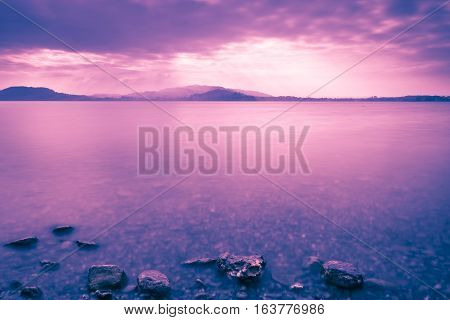 Sunset Lake. On a background the mountains. Tops of stones in water. Play of light and shadow creates a gorgeous volume and distance. Long exposure.