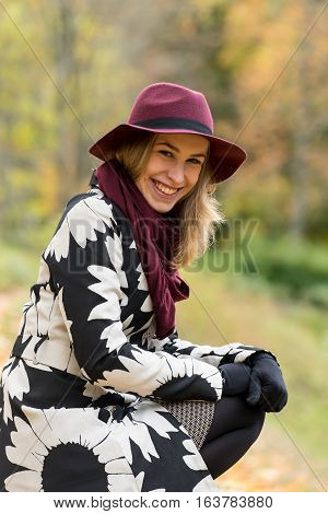 Woman in a floral patterned coat and wine red hat in the park. Happy girl and colorful autumn forest. Portrait of a lady yellow green red and brown leaves background