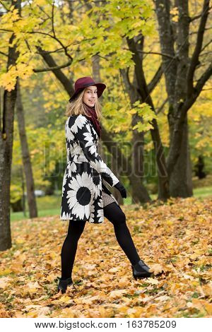 Woman in a floral patterned coat and wine red hat in the park. Happy girl and colorful autumn forest. Portrait of a lady yellow green red and brown leaves background