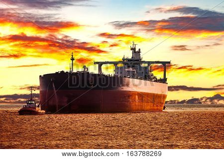 Tanker ship with escorting tugboat on sea at sunrise.