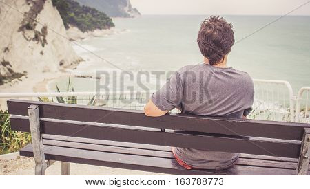 Young Man Sitting On Bench Overlooking Sea