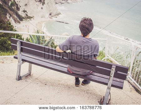 Young Man Sitting On Bench Overlooking Sea