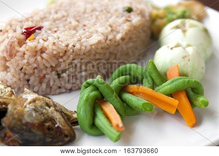 Fried rice with tamarind chili sauce fried mackerel carrot yardlong bean thai eggplant and acacia pennata omelette on white dish and wood table for thai food background