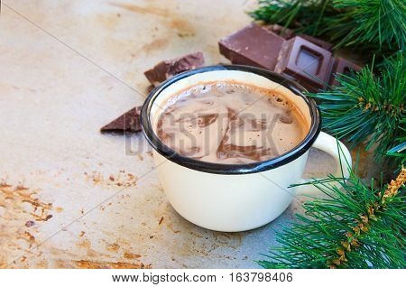 Enamel mug of hot chocolate cocoa and slice of bitter chocolate on metal vintage background with fir tree. Winter times drink concept. Delicious cold weather beverage.Copy space.
