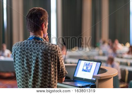 Casualy dressed young millennial expert giving talk at scientific conference. Audience at the conference hall. Business and entrepreneurship event.