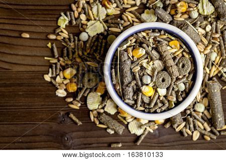 dry food for rodents in bowl on dark wooden background top view.