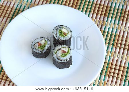 Three portions of sushi rolls with ingredients lies on white plate on wicker kitchen tablecloths. Photo closeup