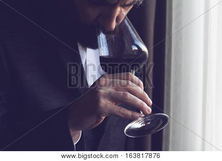 horizontal close up of a Caucasian man with beard black suit and white shirt tasting a glass of red wine