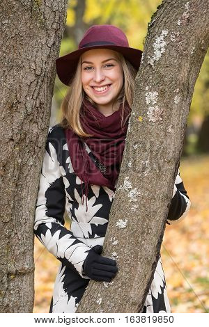 Woman in a floral patterned coat and wine red hat in the park. Happy girl and colorful autumn forest. Portrait of a lady yellow green red and brown leaves background