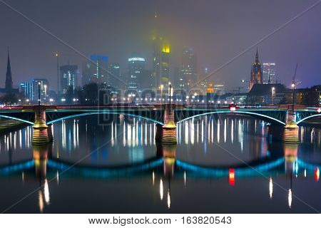 Picturesque view of Frankfurt am Main skyline and Ignatz Bubis Brucke bridge during evening blue hour with mirror reflections in the river, Germany