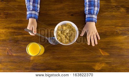 Cute little kid eating corn flakes on breakfast and drinking orange juice