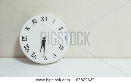 Closeup white clock for decorate show half past six or 6:30 a.m. on white wood desk and cream wallpaper textured background with copy space