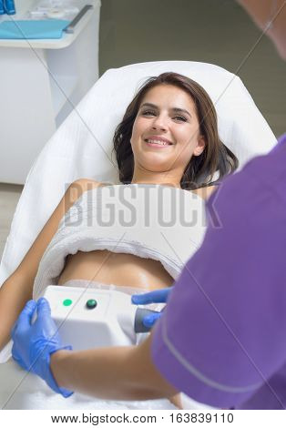 Pretty young woman getting cryolipolyse treatment in cosmetic cabinet
