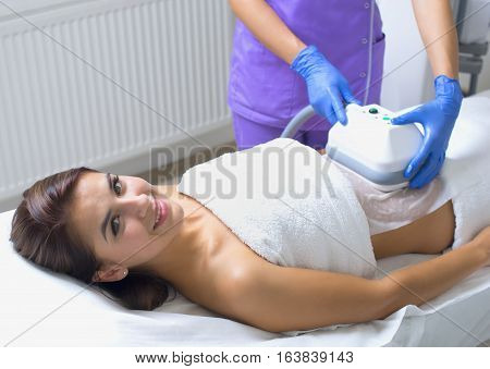 Pretty young woman getting cryolipolyse treatment in cosmetic cabinet