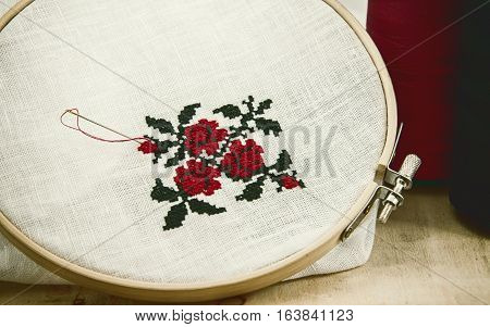 Hand embroidery cross-stitch flower ornament on a white fabric in the wooden embroidery frame red and black thread vintage toning