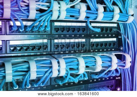 Network switch and blue ethernet cables in server room. Patch cords connected to router in data center. Horizontal technology background with gradient