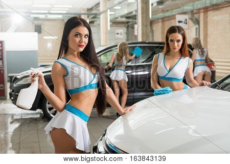 Sexy curly long haired blondes in fromula one style tops and mini skirts posing with pompons near car at carwash