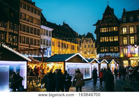 STRASBOURG FRANCE - DEC 20 2016: Famous Christmas Market with Place de la Cathedrale with tourists and locals in front of Notre-Dame Cathedral and iconic maison Kammerzell at dusk