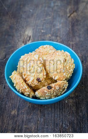 Homemade cornflakes and raisins cookies in a blue bowl on old wooden table with place for text. Freshly baked corn flake cereal cookies on rustic background. Selective Focus. Copy space.