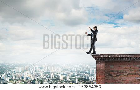 Businessman with blindfolder on eyes walking on building top