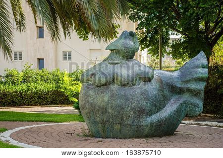 Holon Israel-July 21 2016: Bronze art sculpture Chicken Hen by Yael Artsi is installed under green trees in small city park at Golda Meir Street. Wide shot in bright sunny day on the white residential building background